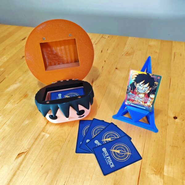 Deckbox Funko Pop de Monkey D. Luffy abierta, mostrando su interior espacioso junto a cartas de One Piece TCG y un soporte azul. Diseño coleccionable inspirado en el protagonista de One Piece.